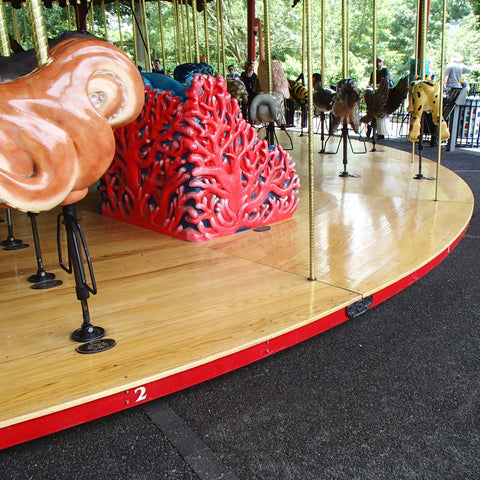 Carousel with wooden horses and a red and black dragon-like creature on a wooden platform.