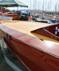 Close-up of a wooden boat with a maroon hull and wooden deck at a marina.