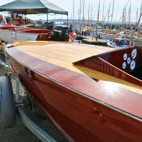 Close-up of a wooden boat with a maroon hull and wooden deck at a marina.