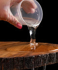 Hand pouring crystal sheen epoxy from a plastic cup onto a wooden surface with a black background