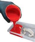 Red silicone mold maker being poured from a container into a mold with a white decorative object.