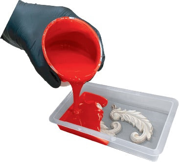 Red silicone mold maker being poured from a container into a mold with a white decorative object.