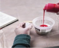 Person pouring quick mold silicone from a bottle into a white container on a light surface.