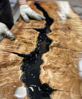 Wooden surface with black resin flowing through it, being worked on by a person wearing gloves.