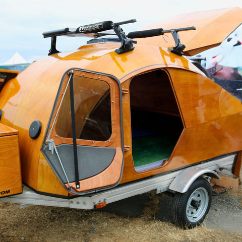 Wooden teardrop camper trailer with a door open, parked on a grassy area.
