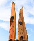 Two orange kayaks standing vertically against a blue sky with white clouds.