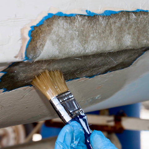 Person painting a wooden surface with a brush, wearing blue gloves.